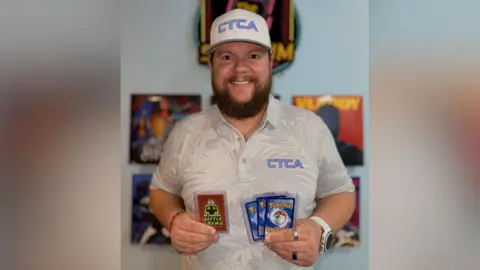 Nick Jarman Nick Jarman wearing a polo top and holding Pok&eacute;mon cards