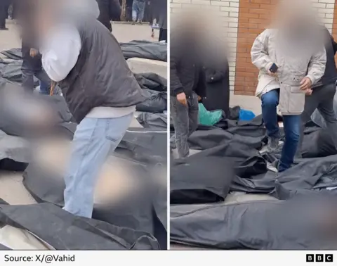 Black body bags that have been blurred to hide the victims' faces and body parts are visible on the ground. Men with faces blurred walk among them appearing to search for loved ones.