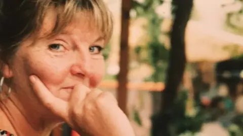 Armstrong family A woman looking sideways at the camera with her hand on her face, smiling