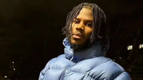 XL Recordings Jim Legxacy pictured outdoors at night in a light blue puffa jacket