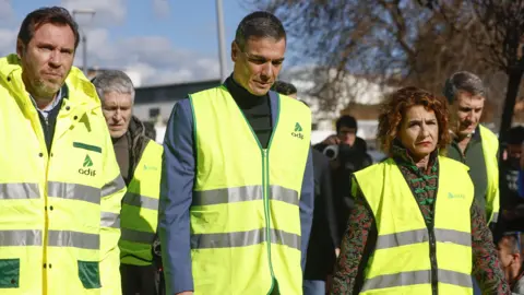 EPA Spain's Prime Minister Pedro Sanchez (centre) arrives with Minister of Transport Oscar Puente (left) and First Deputy Prime Minister Maria Jesus Montero (right) and other officials at Adamuz. All are wearing high-viz jackets.