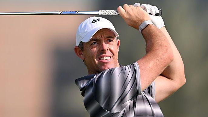 Rory McIlroy watches his shot as he holds a club above his head
