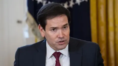 EPA An image of the US Secretary of State, Marco Rubio, speaking into a microphone while wearing a navy suit with a red tie.