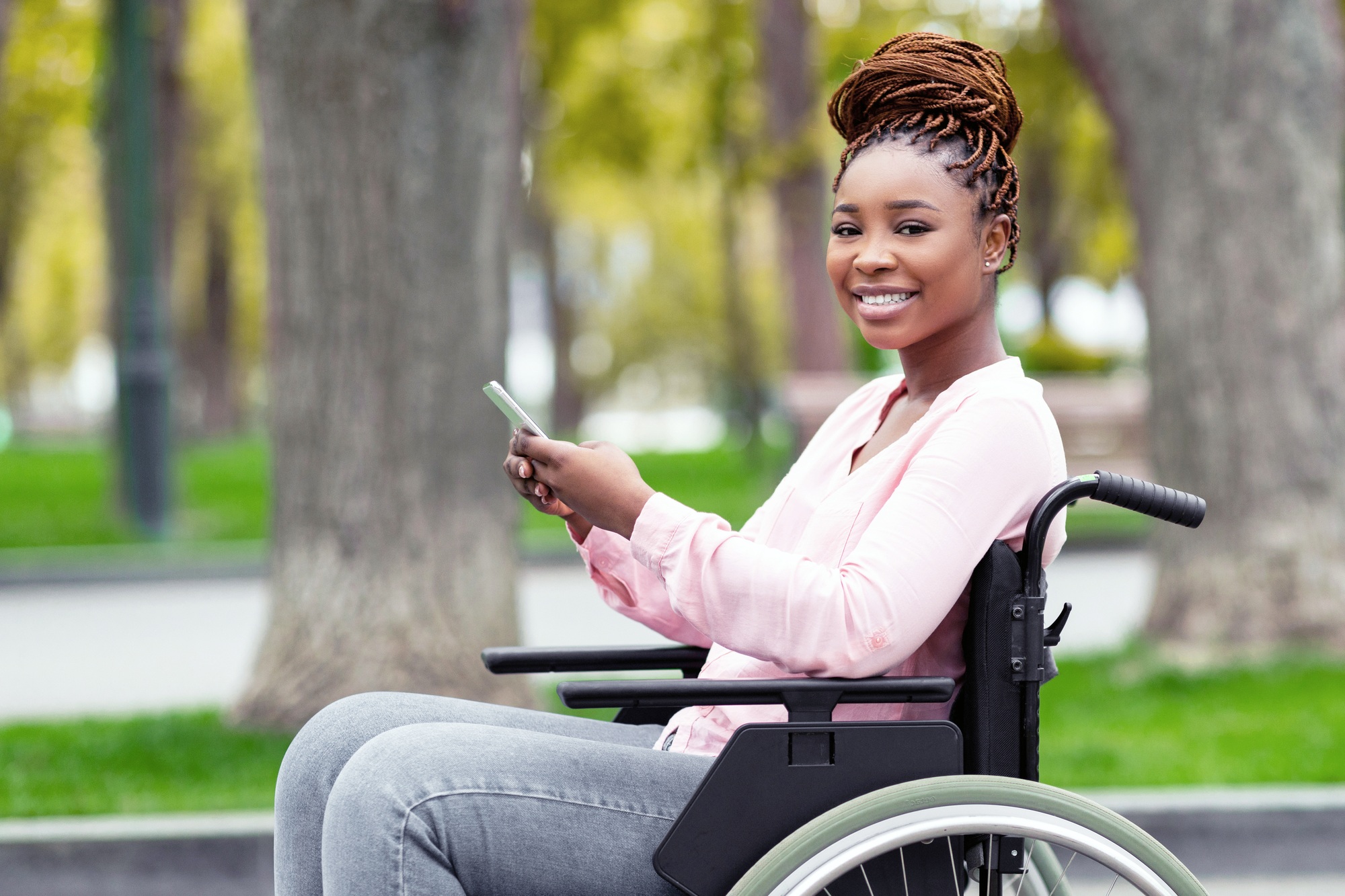 Happy disabled black woman in wheelchair using cellphone, checking social media, browsing web at