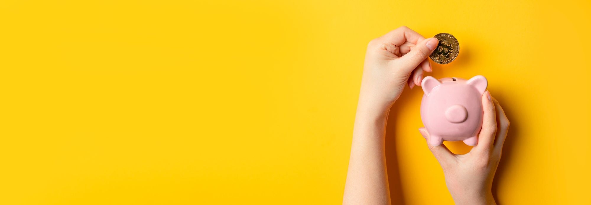Man hand holding bitcoin coin and pig piggy bank on yellow background with copy space.