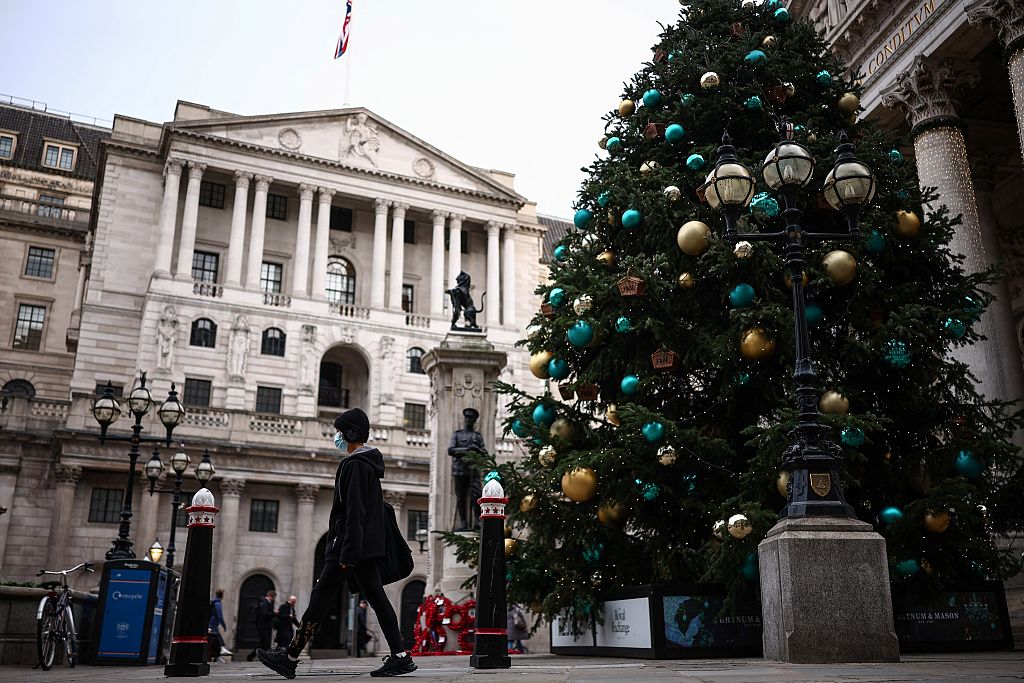 A pedestrian walks past the Bank of England (L) and a Christmas tree set up in front of the Royal Exchange building (R) in central London on December 12, 2025