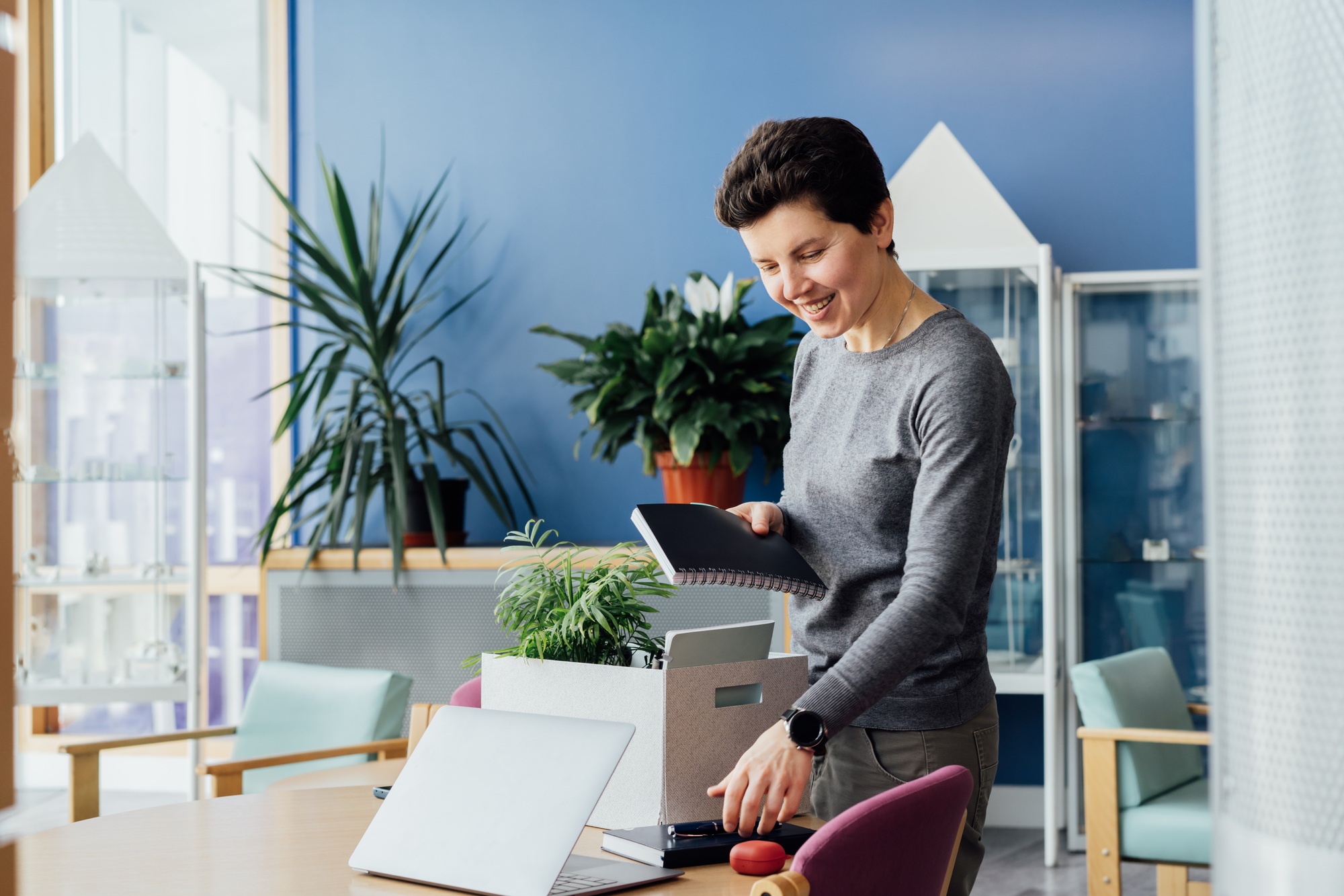 Satisfied newcomer middle aged neutral gender female worker unpacking box at new workplace