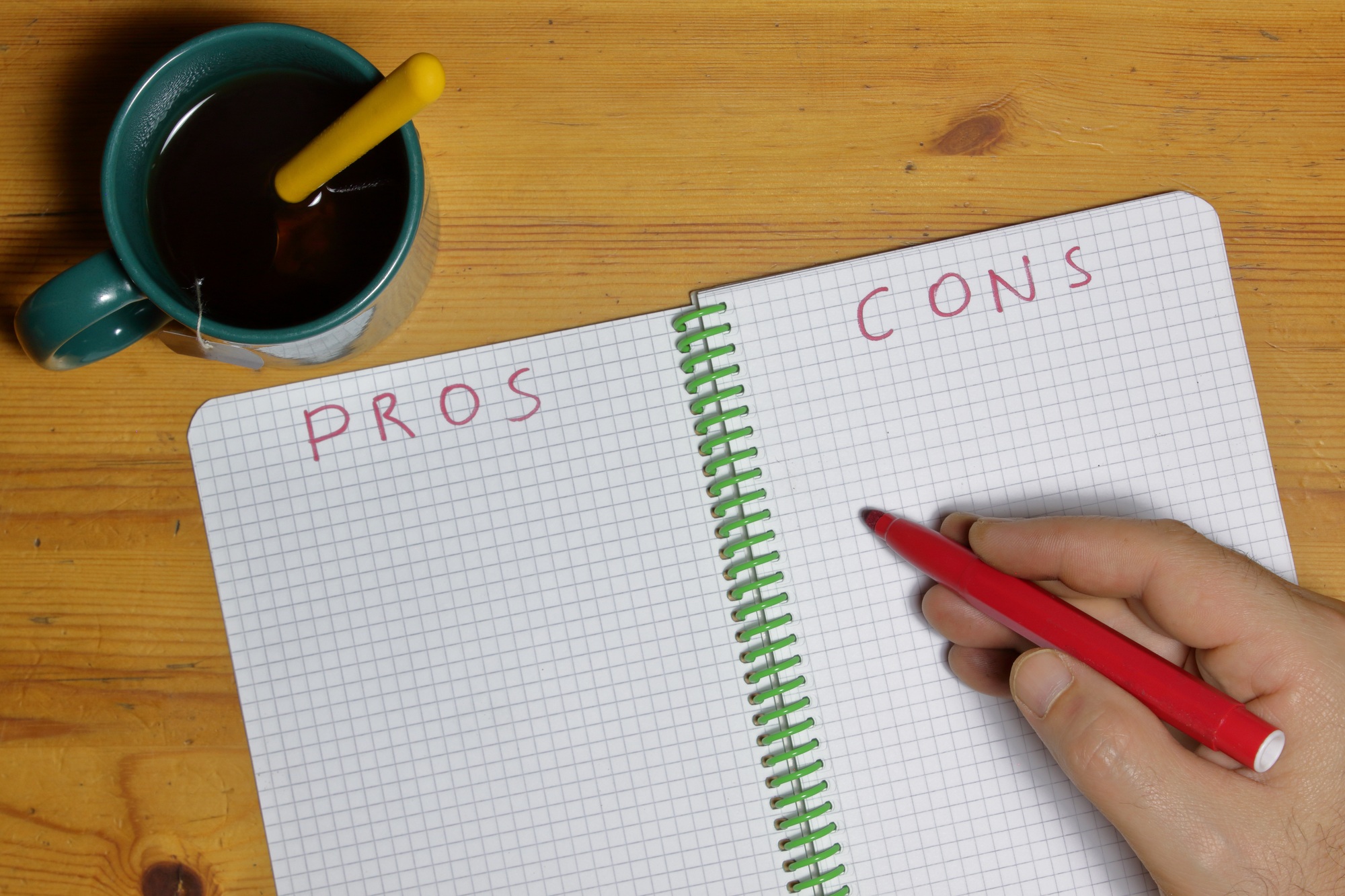 Top view of a notebook for determining pros and cons with a cup of tea