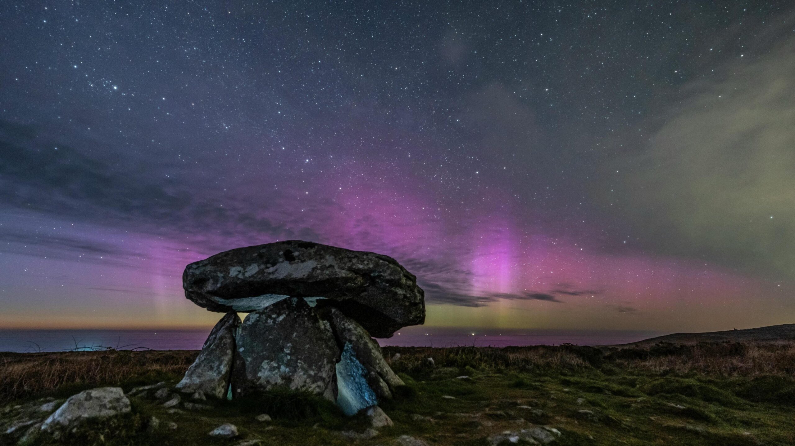 image of a rock with cloud and purple colours of the aurora in the night sky.