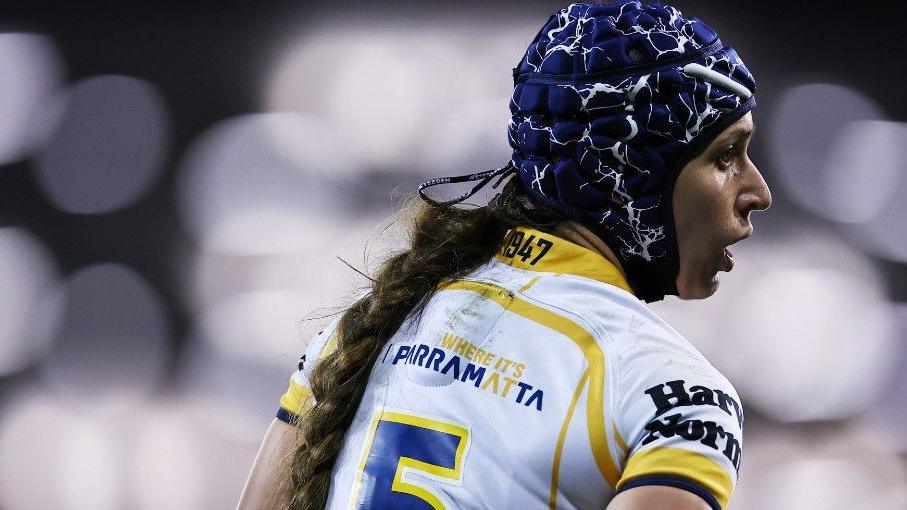 Monique Donovan pictured mid-game wearing a scrum-cap and long pony-tail, in a match-fit Parramatta Eels player jersey.