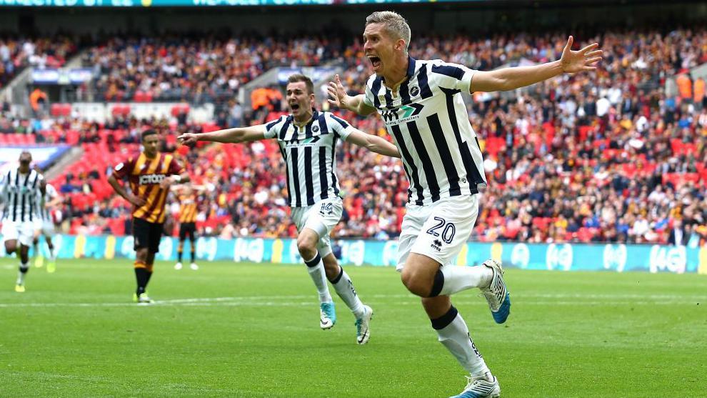 Steve Morison celebrates, running with his arms outstretched along the touchline of the pitch at Wembley Stadium, with players running behind him to congratulate him