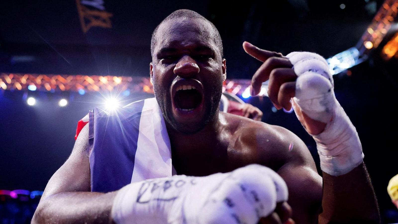 Daniel Dubois leans over the ropes of a boxing ring and holds up his hand