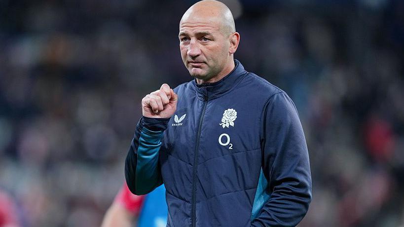 Steve Borthwick, wearing a nany blue zip-up England jacket, looks into the distance, his right hand raised to shoulder level