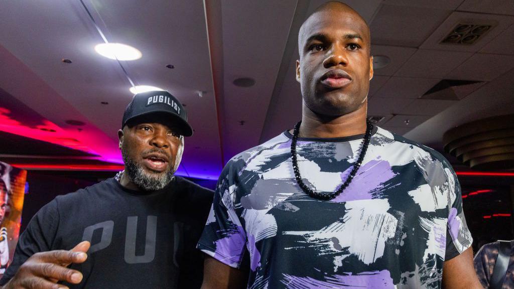 Don Charles (left) wearing a black t-shirt and baseball cap is next to Daniel Dubois (right) who is wearing a patchwork white, black and purple t-shirt