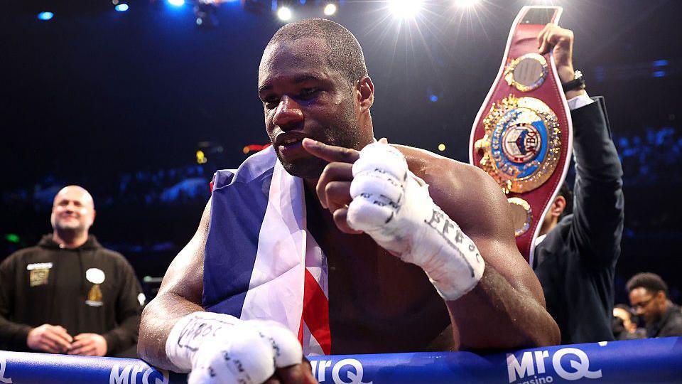 Daniel Dubois leans over the ropes of a boxing ring and holds up one finger