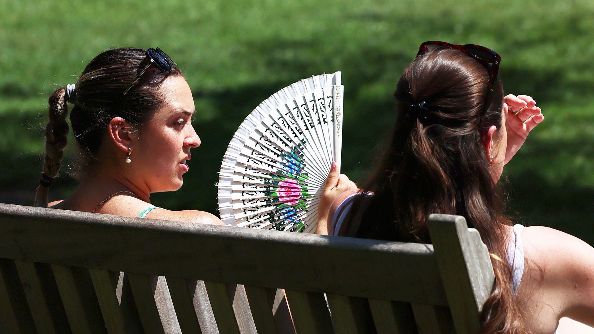 A woman uses a fan to cool down at a park in London, Britain, 24 June 2026.