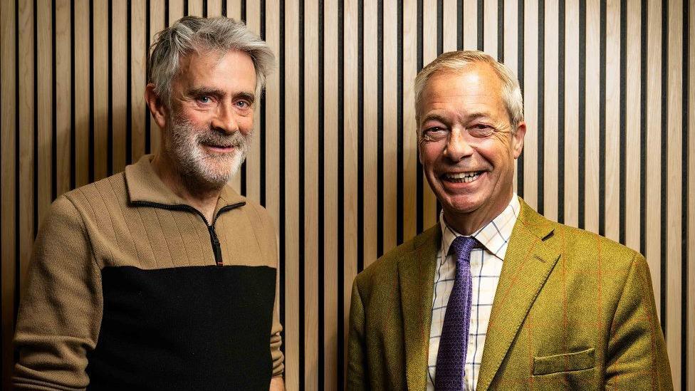 Christopher Harborne, left, wears a beige and black jumper. He has a full head of grey hair and a grey beard and bushy eyebrows. He stands next to Farage who is grinning. Farage is wearing a green suit and checked shirt and purple tie.