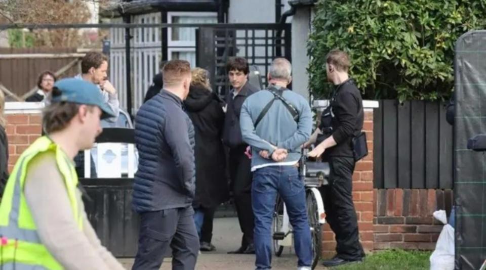Paul Mescal is dressed in a blue jacket black trousers on a film set outside a beige coloured semi detached house.