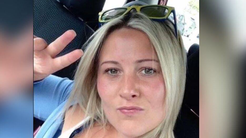 A woman with blonde hair is looking at the camera, holding up two fingers