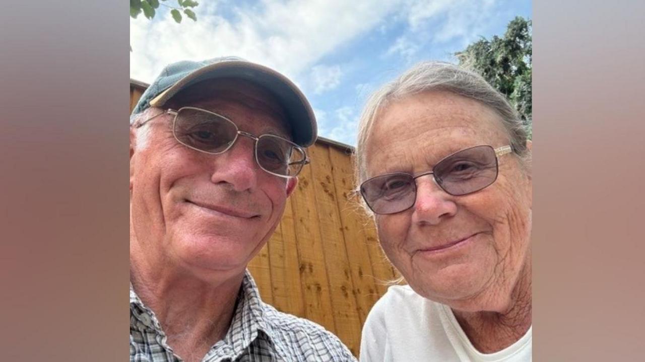 A selfie-style image of an elderly man and an elderly woman. They are wearing glasses and smiling while looking into the camera. The man is wearing a baseball cap. They are both wearing glasses.
