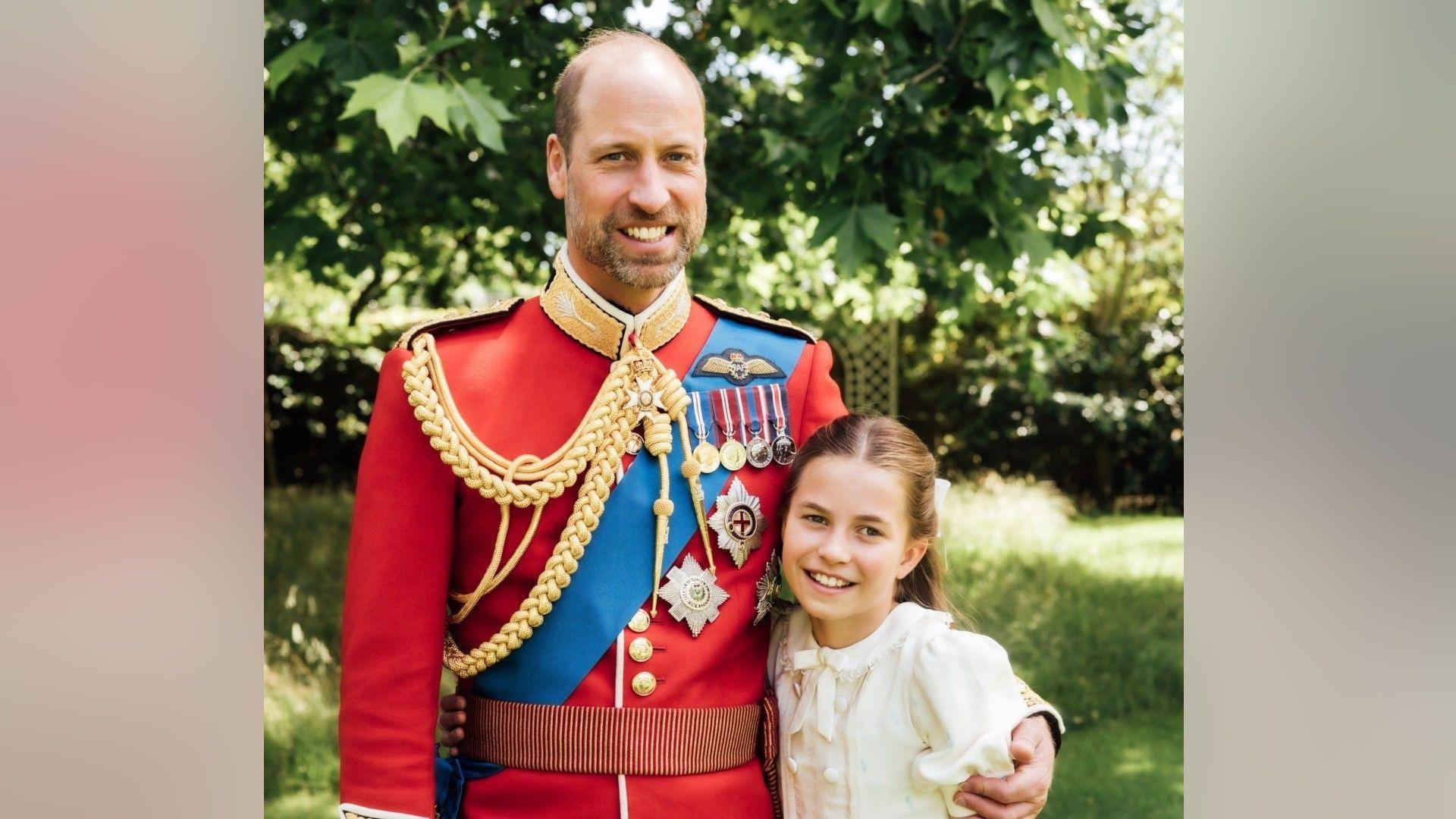 Prince William is wearing the scarlet dress uniform of the Welsh Guards, of which he is colonel, and has his arm around Charlotte, who is wearing a cream dress.