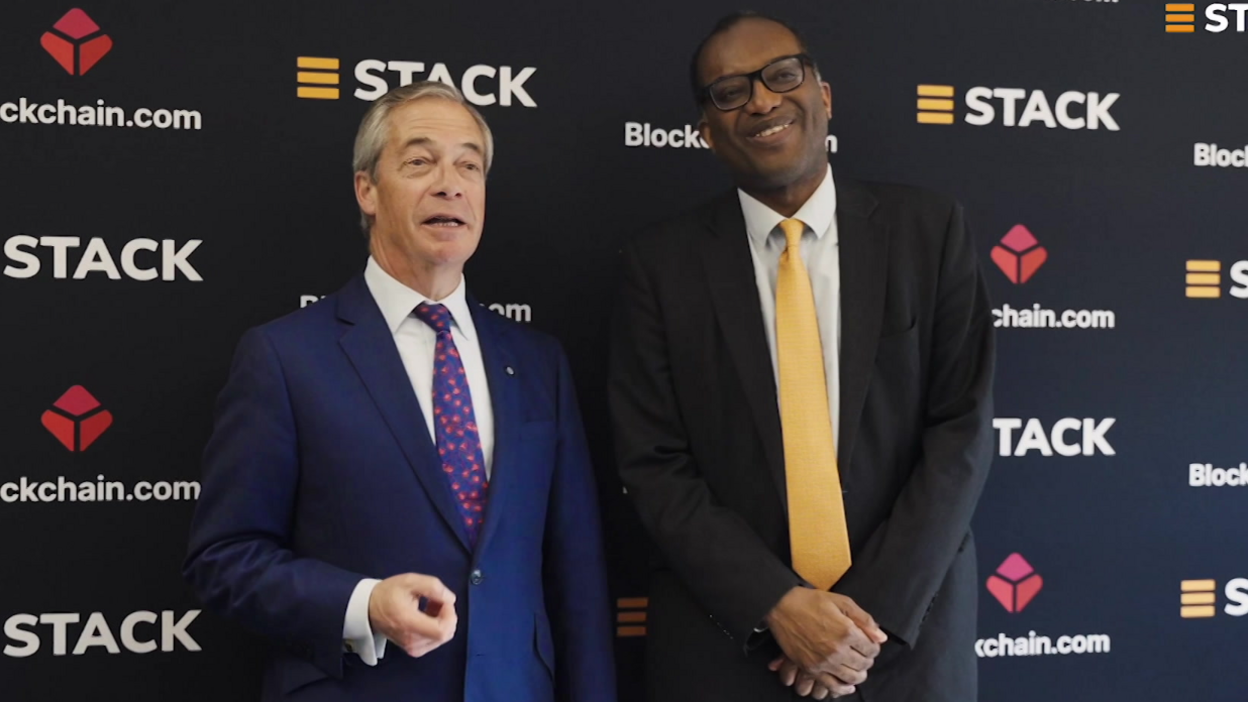 Reform UK leader Nigel Farage (L) stands with former Chancellor Kwasi Kwarteng (R) as they promote cryptocurrency. Farage wears a dark blue suit, a white shirt and a blue tie with red blossoms. Kwarteng wears a black suit,  a white shirt and a butter yellow tie.