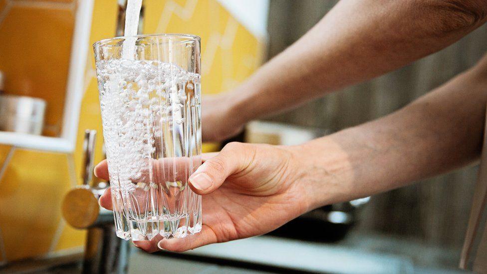 A woman fills a clear drinking glass with water under the tap.