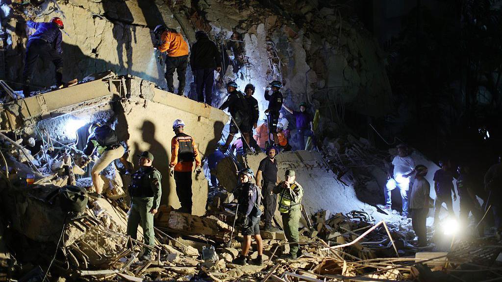First responders attend a damaged building at Los Palos Grandes at night.