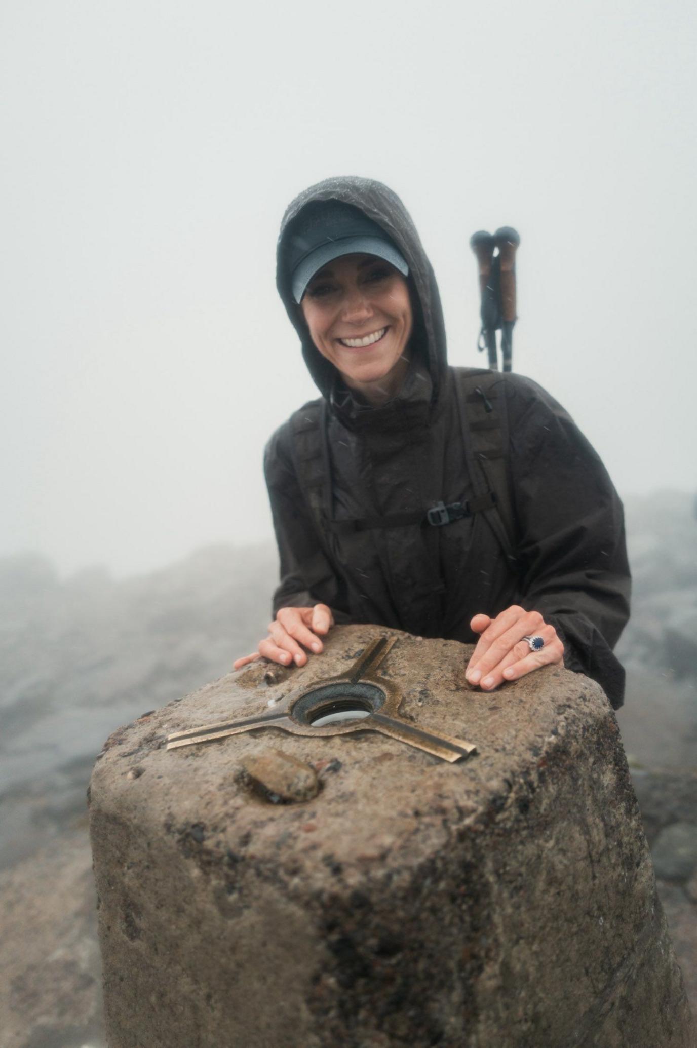 Catherine stands in a raincoat the summit of Ben Nevis