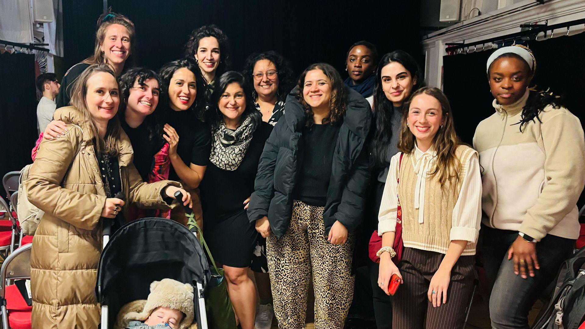 A group picture of 12 women smiling at the camera. The woman on the far left has a pushchair with a baby in it.