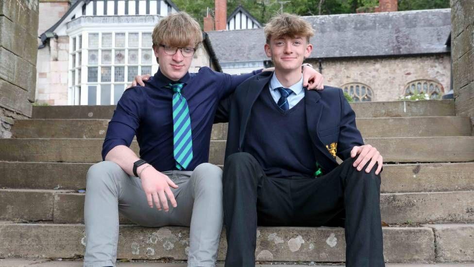 A man with brown hair and glasses, wearing a blue shirt with a stripey tie, next to boy with also brown hair