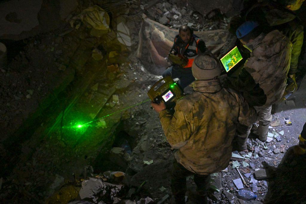 A rescuer wearing a hat and coat uses thermal imaging equipment at an earthquake site in Turkey.