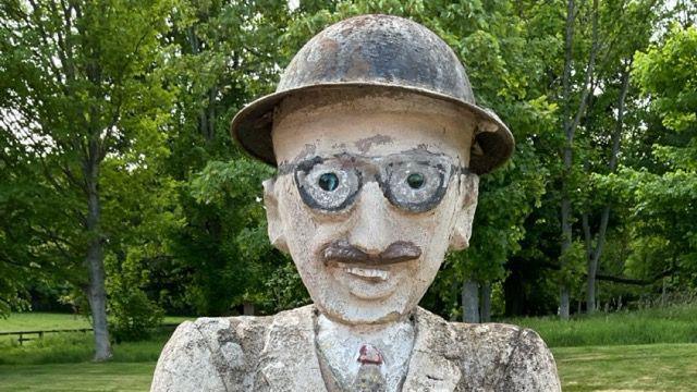 A statue of a man in what looks like a protective hat with glasses and a moustache wearing a suit and tie