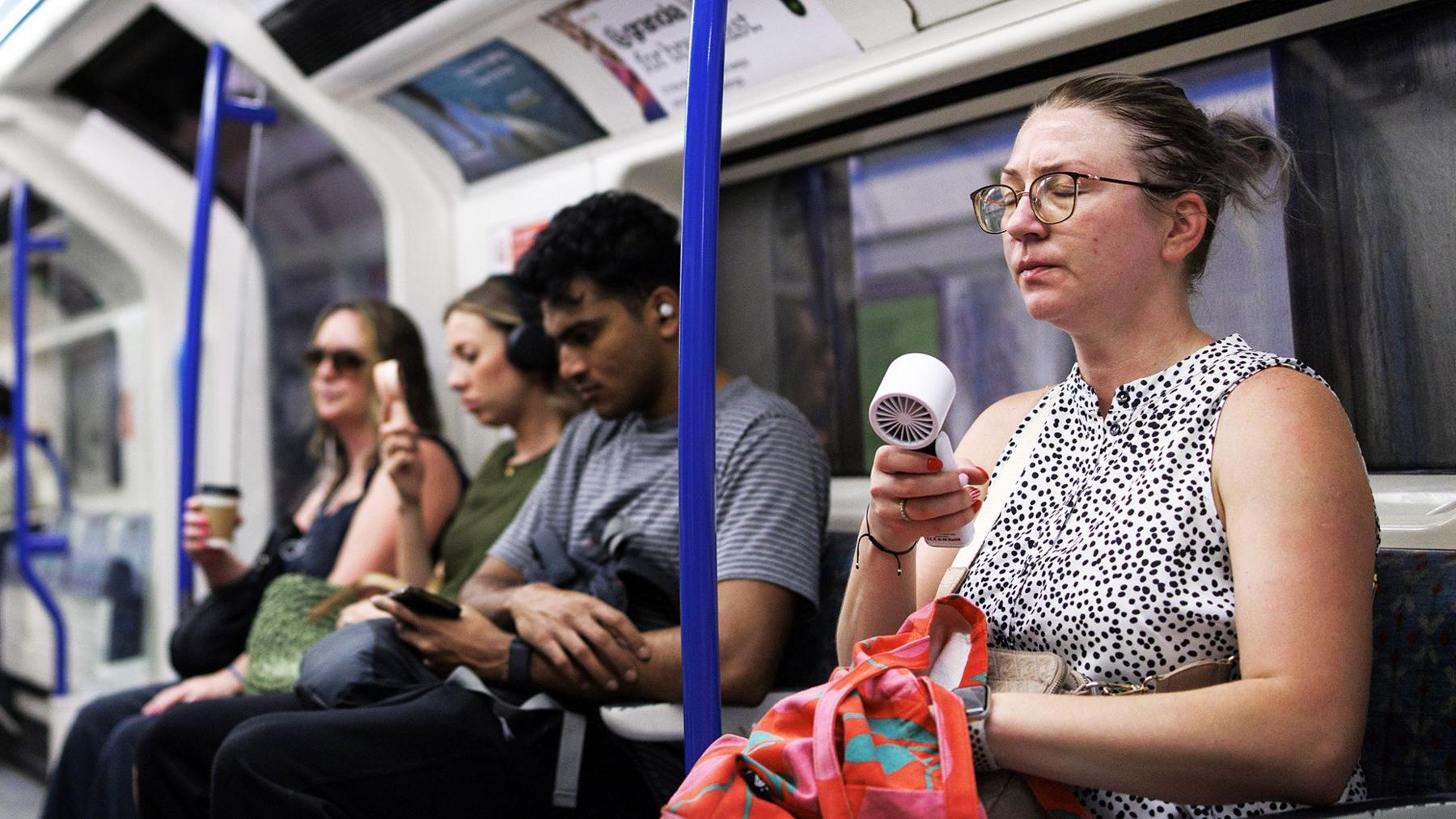 A person uses an electric fan to cool down as commuters travel on the London Underground as the UK is set to experience its hottest June day on record during a heatwave in London, Britain, 24 June 2026. T