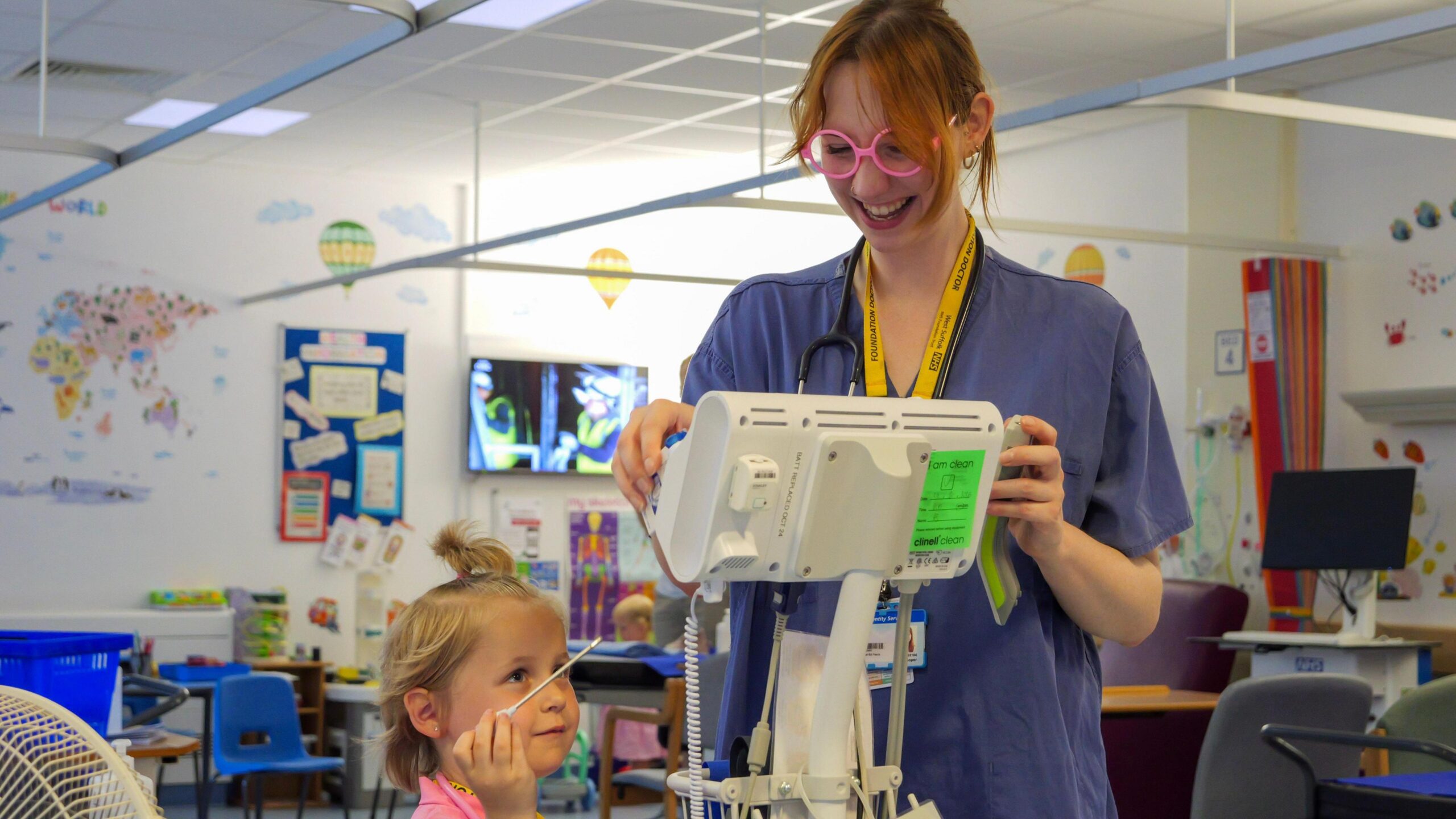 A young blonde girl and a nurse in a hospital room tinkering with a piece of medical equipment.