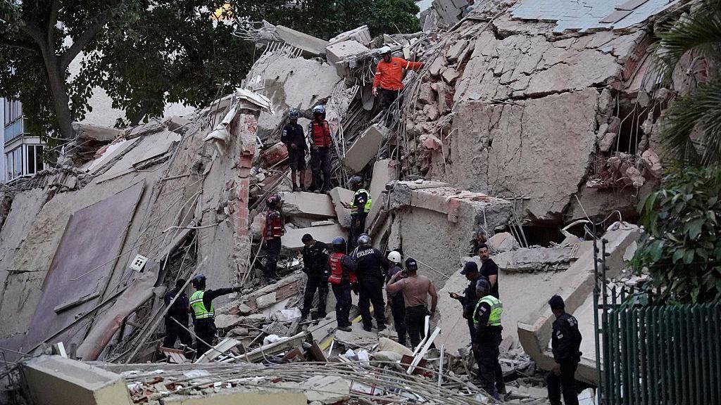 About a dozen rescuers search for victims amidst a building that's been reduced to rubble following an earthquake in Caracas