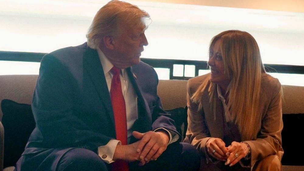 US President Donald Trump speaks to Italian Prime Minister Giorgia Meloni - they are both sitting, with their hands in front of them - Meloni is smiling at Trump, who is in side profile