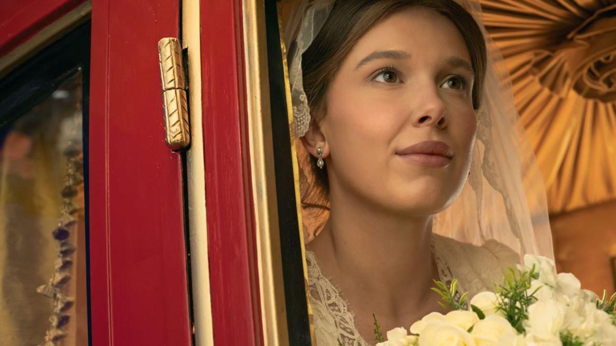 Millie Bobby Brown as Enola Holmes wearing a wedding dress and holding flowers