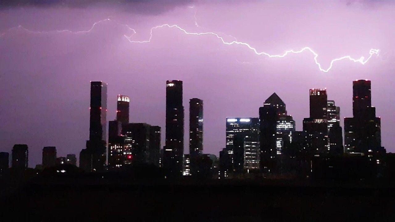 A violet, purple sky with a streak of fork lightning going across tall buildings in London
