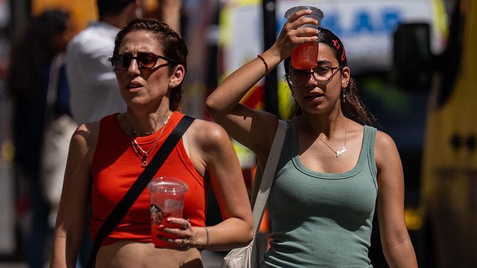 A woman cools her head with an iced drink as she walks through central London  on a sunny day.