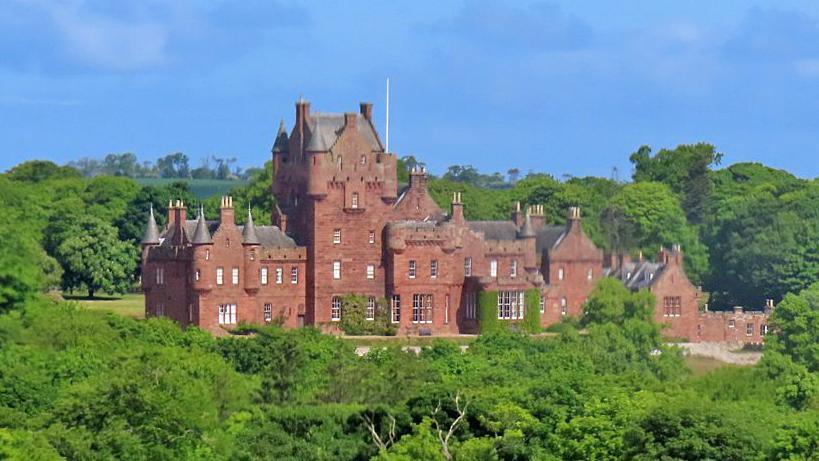 A red stone castle set among plentiful green trees