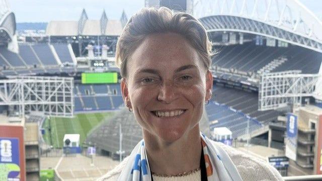 Jess Fishlock smiling and wearing a football scarf with Seattle Stadium in the background