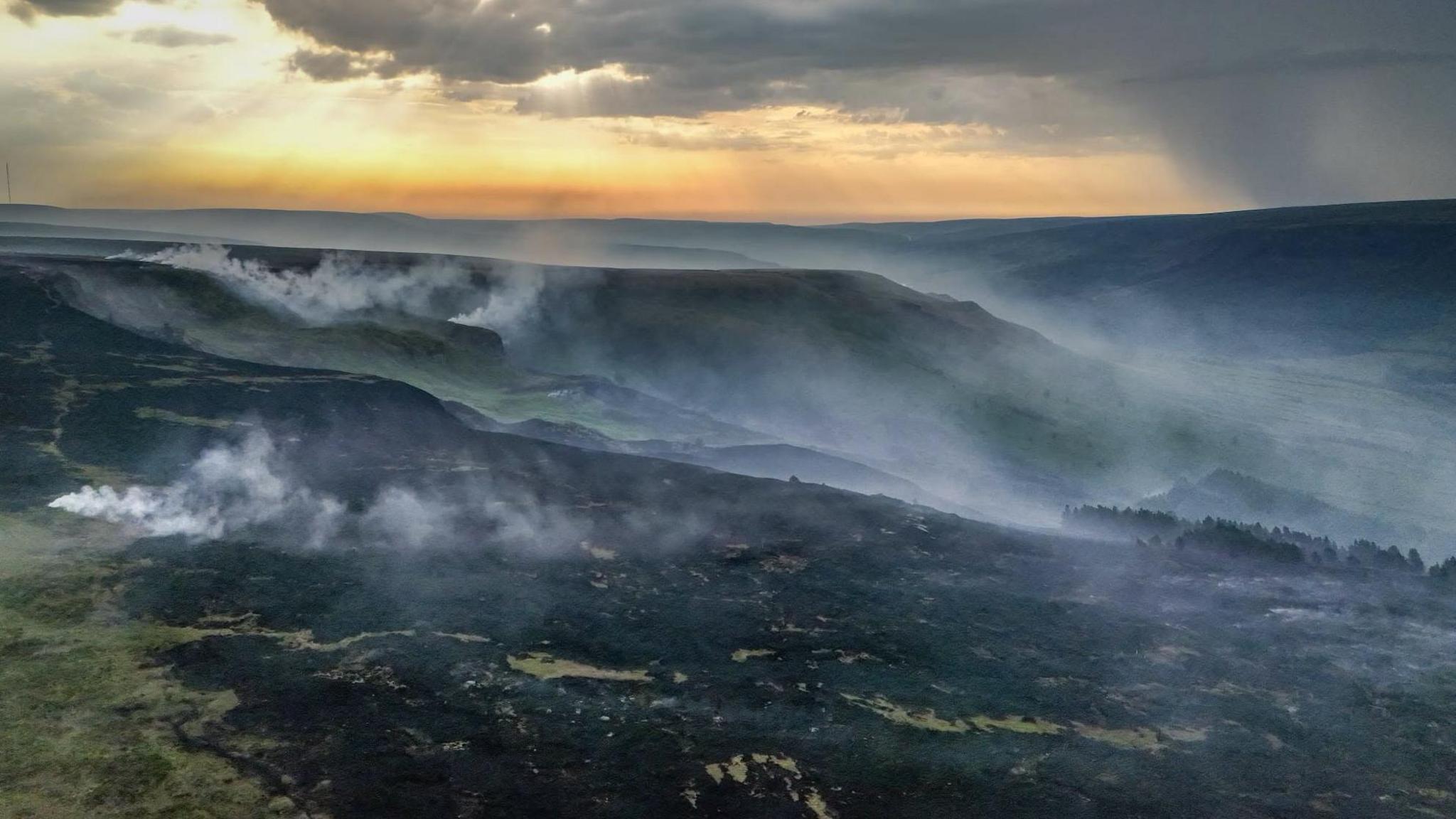 Shot of rolling moorland hills which are blackened and smoking