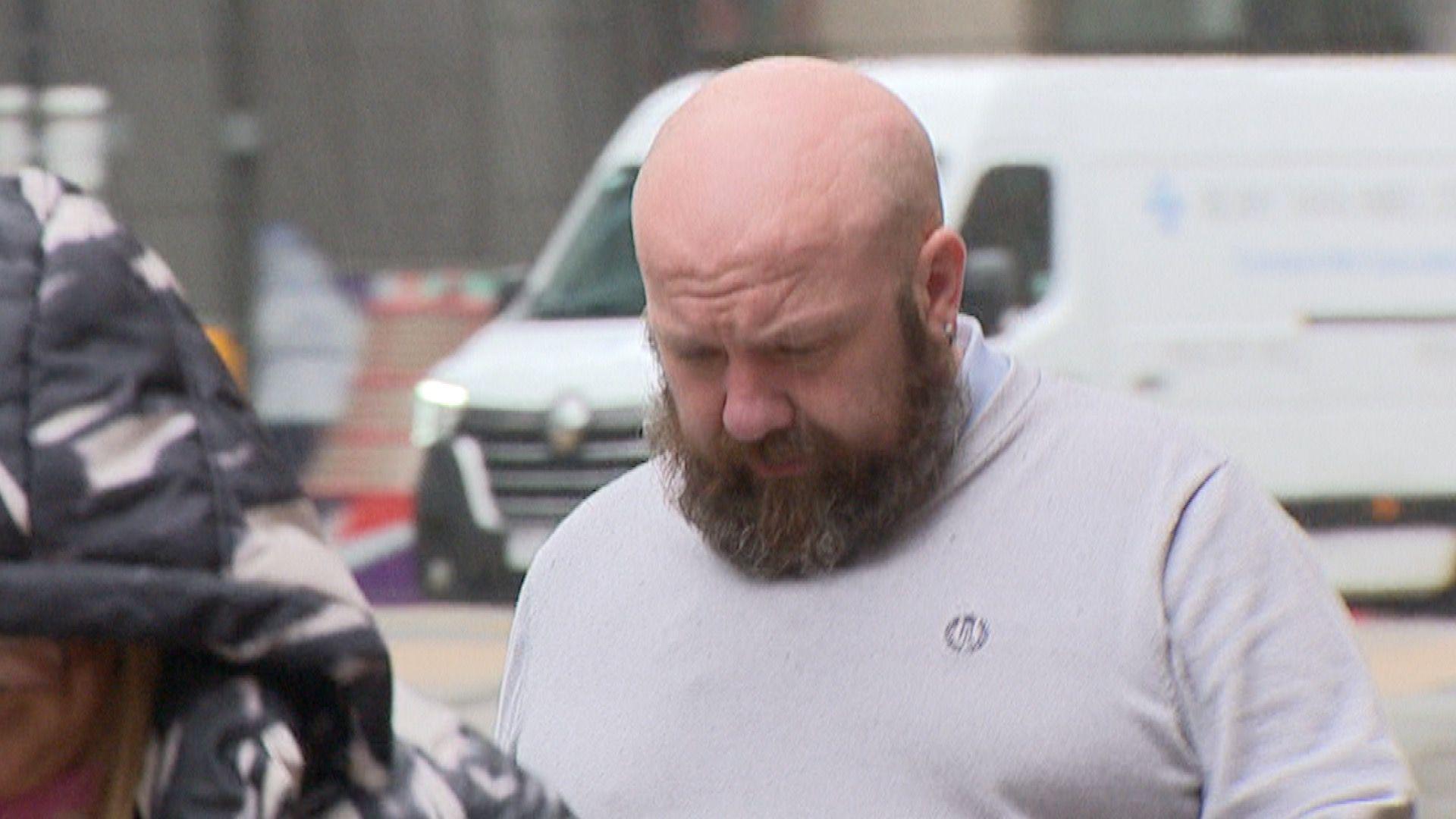 Alan Keelan arriving at court wearing a light grey t shirt. He has a bald head and a light brown beard.