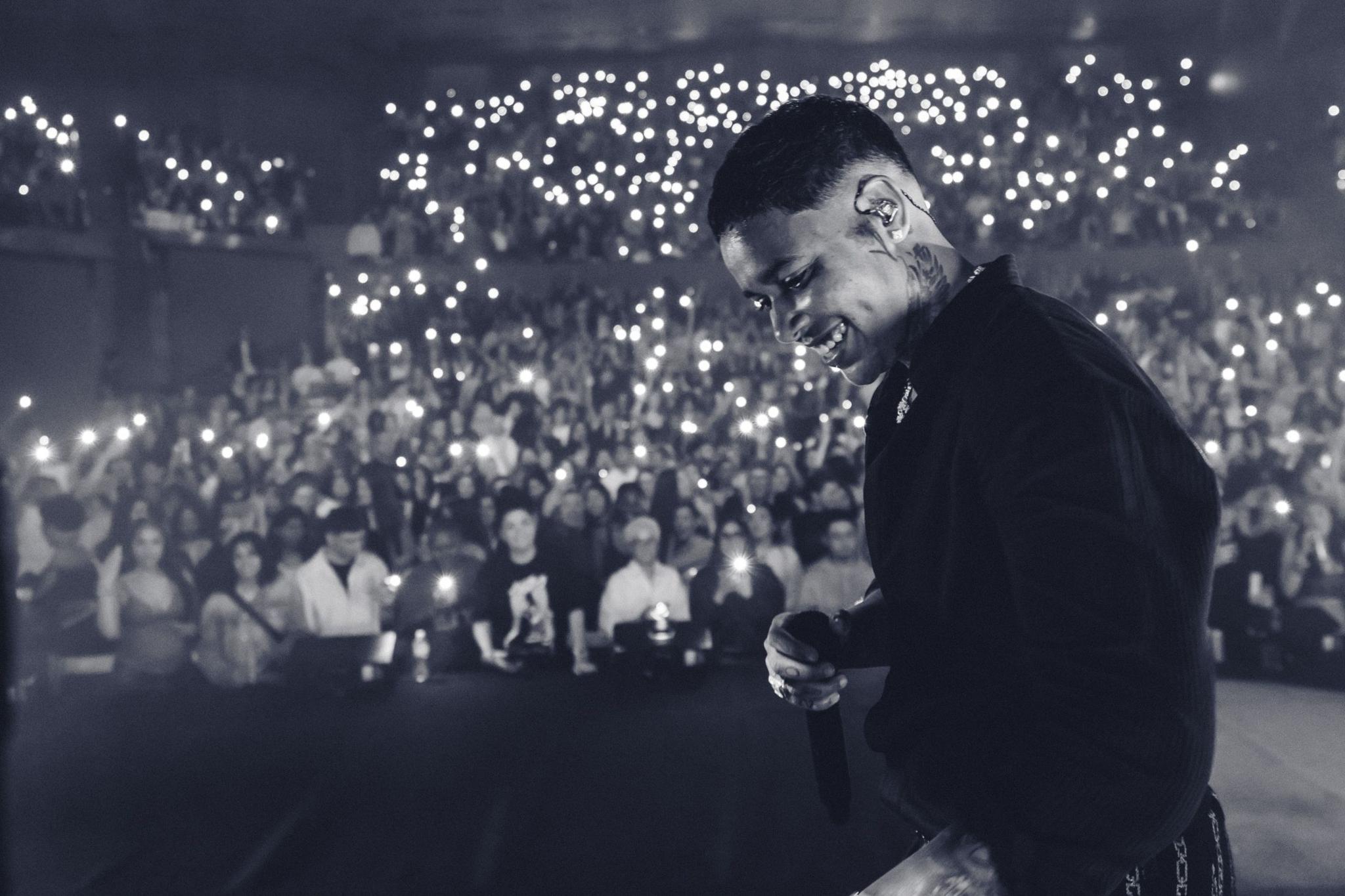 A black and white shot shows KWN performing at Sydney Opera House with a smile on her face, as fans in the audience turn on the lights on their phones.