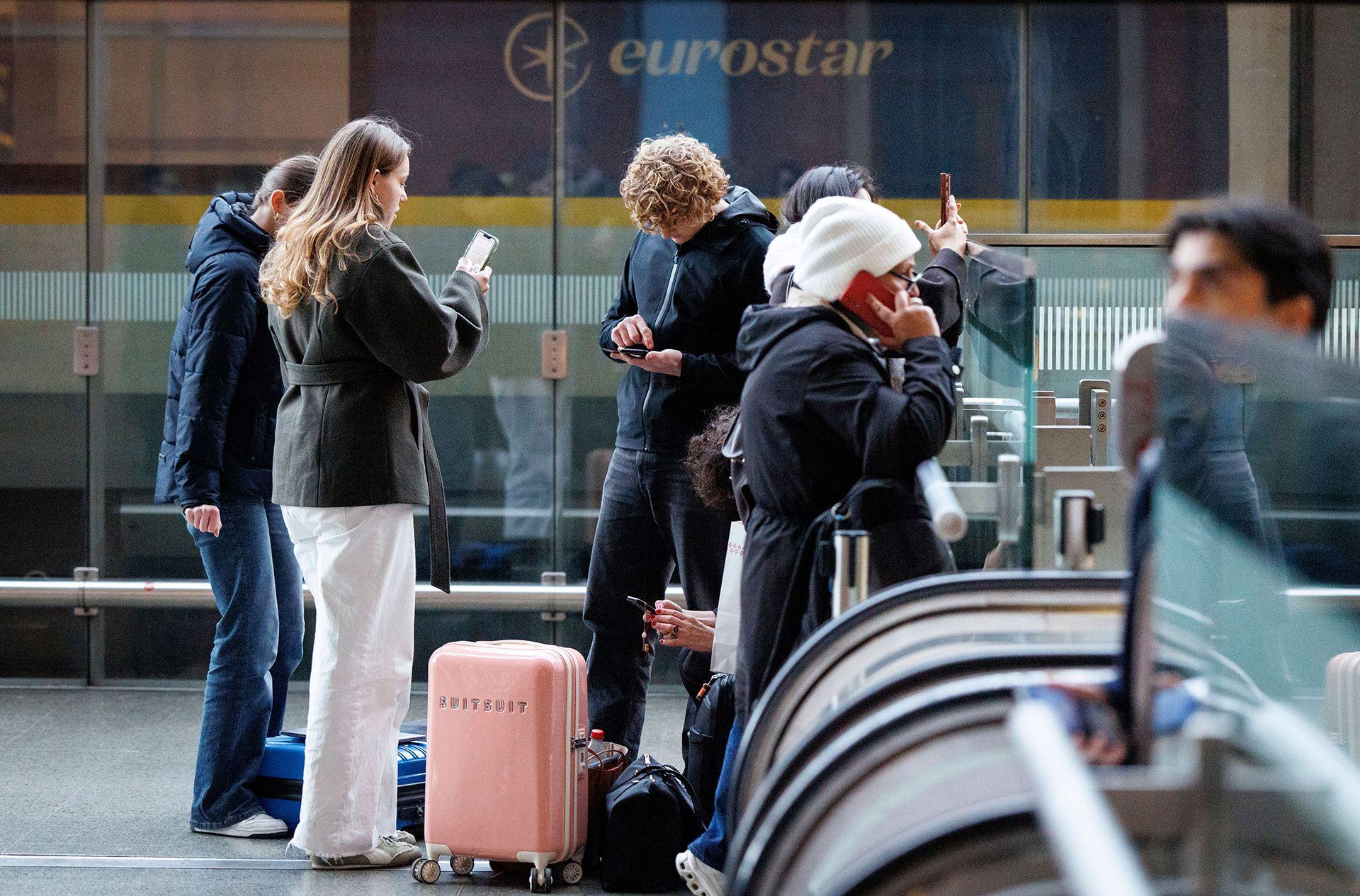 People wait at the top of escalators with luggage and checking phones at the Eurostar terminal at St Pancras in London, in December. The Eurostar sign can be seen in the background.