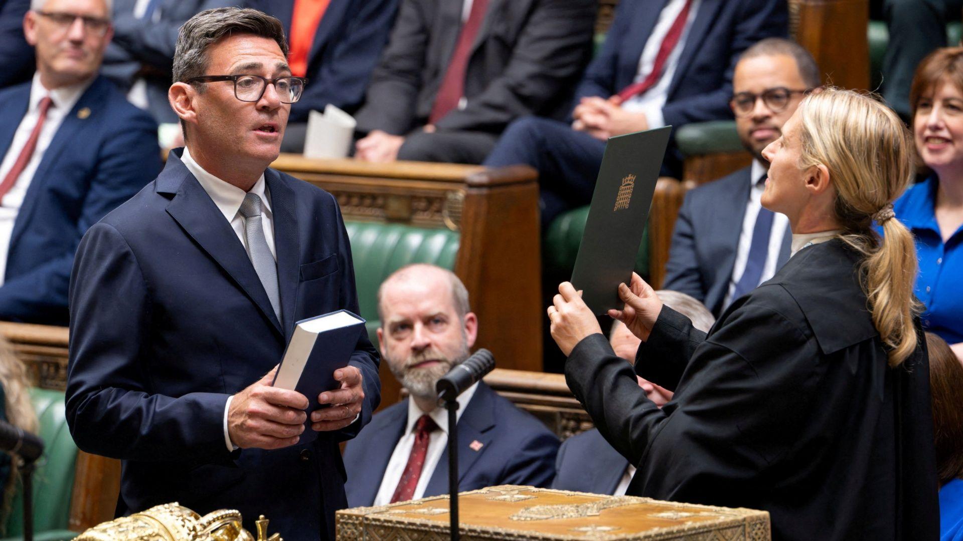 Member of Parliament (MP) for Makerfield, Andy Burnham, is sworn in at the House of Commons, in London. Labour MPs in smart dress sit on the green benches behind him