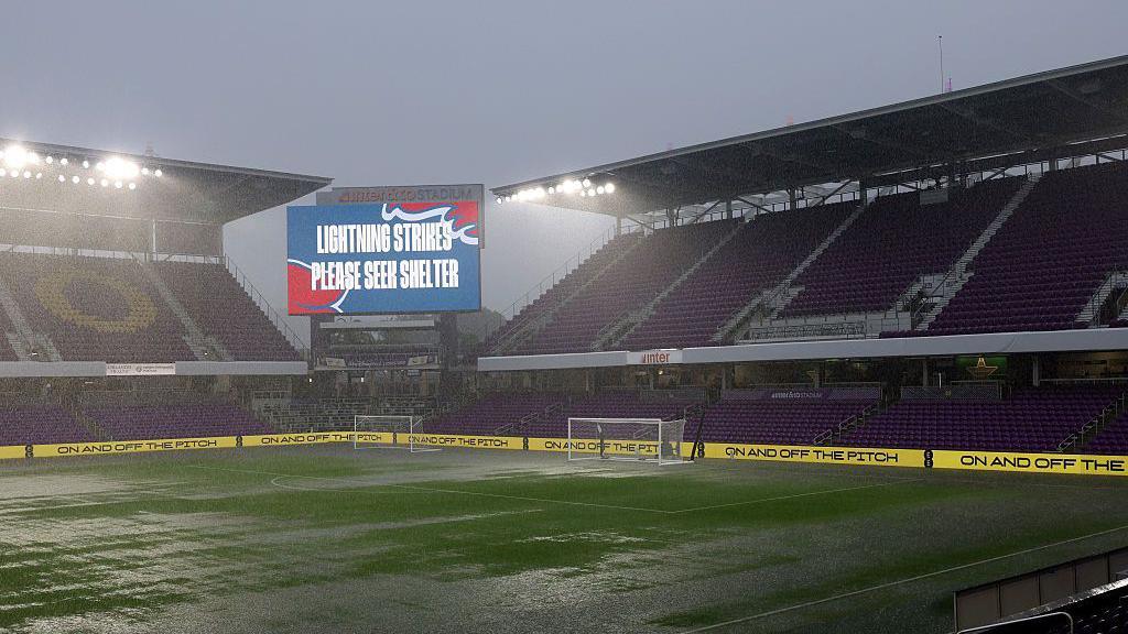 view of a stadium with heavy rain flooding part of the pitch. The big sign says lightning strikes, please seek shelter