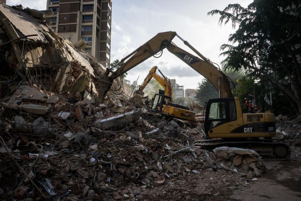 Yellow bulldozers at work next to the debris of a building in Caracas.