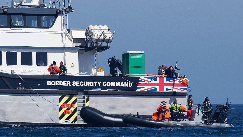 Life vests are thrown back to the French Navy by the UK border force after a 'small boat' crossing on April 27, 2026 in Dover, England. A large Border Force boat is positioned next to a smaller boat in the open sea.